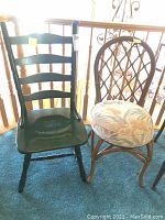 View of black wooden ladder-back chair beside rattan chair with floral cushion, showing the condition and style of both chairs