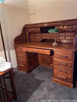 Front view of the oak reproduction roll-top desk showing the brass hardware, carved wood drawer pulls, and included key on the drawer lock.