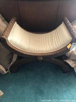 Front view of curved Roman style wooden bench with cream fabric seat, showing the overall shape and carved details.