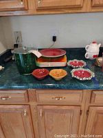 Overview of colorful serving pieces on countertop showing plastic container, melamine trays, leaf-shaped bowls, watermelon-themed bowls, and teapot.