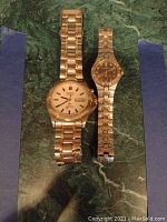 Photo showing both Seiko watches, men's larger model and women's smaller model, side by side on green marble surface