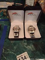 Two Denver Broncos logo wristwatches in black presentation boxes with white interiors.