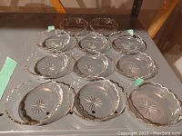 Eleven antique cut glass dessert dishes displayed in two rows, showing clear starburst cuts and scalloped gold-rimmed edges.