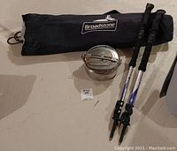 Broadstone camp table in black storage bag, pair of Black Diamond walking sticks, and stainless steel nesting cooking pots displayed on floor.