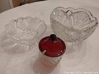 Two clear crystal bowls and one lidded sugar bowl with ruby red lid displayed on a patterned tablecloth