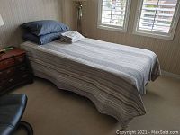 Bedroom setup showing extra long twin bed with striped coverlet and pillows