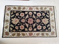 Top down view of the hand woven area rug showing general floral pattern and black background with light floral border and fringe.