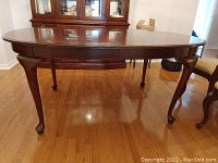 Front view of oval cherry extension dining table without leaves showing cabriole legs and pad feet