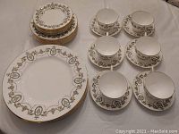 Stacked plates, teacups, and saucers arranged on a table, showing decorative pattern and gold rims
