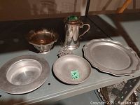 Photo showing the five pewter pieces arranged on a shelf with good lighting to display size and form.