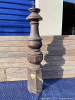Full view of tall wooden newel post showing the angular facets at the base and turned midsection with a rounded top.