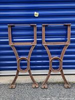 Front view of the pair of antique cast iron workbench legs with three-pronged feet and circular central support.