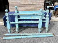 Full view of disassembled antique wooden rope bed frame painted blue, showing headboard, footboard, and side rails.