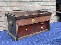 Angled view of the wooden toolbox showing the front panel with four drawers and white ceramic knobs, as well as the overall rectangular box shape with wooden lip.