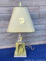 Full view of the lamp showing the beige conical lampshade and green ceramic figurine base depicting an Asian woman in traditional attire