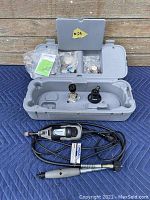 Overview of case opened showing rotary tool, flexible shaft attachment, tool stands, and compartments with accessories packed inside plastic bags with user manual.