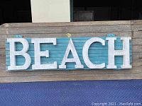 Front view of the entire wooden BEACH sign showing the blue slatted background and large white 3D letters.