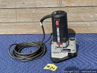 Full view of the laminate trimmer with cord coiled next to it on a blue mat, black top with red button, Porter Cable logo on side.