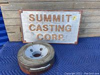 Wooden industrial foundry sign propped behind a circular sand casting mold on a blue blanket against wooden wall.