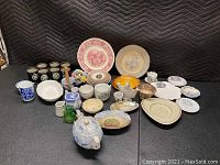 Full overview of approx. 30+ English, Japanese, Denmark vintage china plates and ceramic pieces on table with protective blanket background