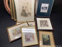Grouped view of multiple framed artworks in varying sizes with diverse styles including figurative, abstract, and landscape images, some with color and some black and white, displayed standing upright on the floor.