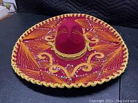 Photo showing front side of the burgundy Antoni's Mexican sombrero with gold and orange embroidered patterns and silver sequins, with gold braided brim.