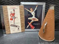 Front view showing two vintage cheerleader advertisement pictures and the leather-covered megaphone with metal rim and handle.