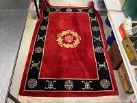 Full view of the rectangular rug laid out, showing its red center and black border with Chinese symbolic patterns.