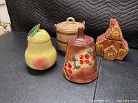 Four cookie jars circa mid 20th century on black surface, pear-shaped, berry decorated, barrel and house shaped.