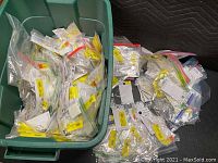 Wide bin filled with hundreds of individually packaged pieces of costume jewelry in plastic bags with yellow labels.