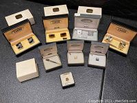 Overview of eight Lamode cufflinks and tie pins in original boxes on black surface.