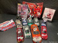 View showing nine NASCAR diecast cars in various colors with Dale Earnhardt and Dale Jr. imagery, framed photo, mini hood, Coca-Cola globe, and magazine.