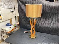 Full view of the Danish style mid modern sculpture lamp with round fabric drum shade, sculptural wooden base, and metal base plate on a black table.