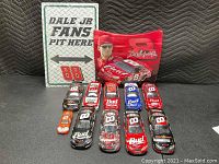 Overview of all items including 10 cars, mini hood, and metal wall sign arranged on black surface