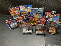 Overview photo showing 13 packaged racing die-cast cars from Racing Champions, Hot Wheels, Johnny Lightning, and others arranged side by side on black surface
