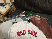 Wide angle shot showing four jackets and vest laid out on a bed: two black leather jackets, one brown leather vest, and one white Red Sox jacket.