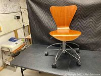 Front view of mid century modern wooden swivel chair showing wood grain seat and backrest, metal base, and casters.