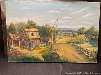 Photo of signed Hiriko painting depicting rustic road with older houses, greenery, and a car under a mostly cloudy sky.