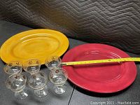 Two large handpainted platters in mustard yellow and dark red with a tape measure showing length around 18 inches, accompanied by six decorative stemmed glasses with fall leaf motifs.