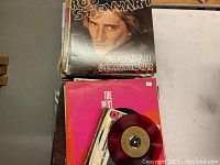 Stack of vinyl records showing the Rod Stewart album 'Foolish Behaviour' on top with a visible red 45 RPM single.