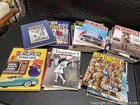 Top view showing multiple stacks of Reminisce magazines with colorful nostalgic and vintage themed covers along with hardcover books related to vintage and collectibles.