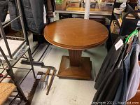 Top view of round wood table showing table top surface and surrounding environment with nearby clothing and stored items.