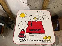 Top down view of Snoopy themed kids table showing cartoon artwork of Snoopy on doghouse with Woodstock and Charlie Brown characters