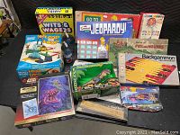 Overview photo of the lot showing multiple boxed games and toys including Loop Loop, Simpsons Jeopardy, Fox and Hounds, Backgammon, Star Wars puzzle, and dinosaur toy in box.