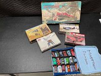 Overview of vintage Matchbox cars in blue collector mini-case alongside several unopened model kits and wooden ship construction kit on black surface