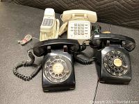 Four vintage phones including two black rotary dial phones and two beige push-button phones on a dark surface.