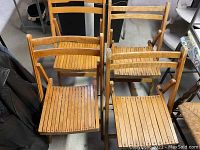 Four vintage wooden folding chairs arranged in a group, showing the slatted wood seats and backs.
