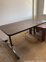 Adjustable height table with dark wood top and black metal legs shown near wall and floor, wires on floor