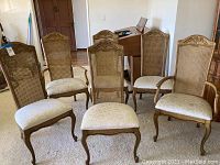 Front view of all six cane back dining chairs arranged in a row showing wooden frames, cane backs, carved tops, and upholstered seats.