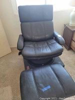 Black leather recliner chair with matching ottoman shown from front angle, leather upholstery visible with some wear and creases.